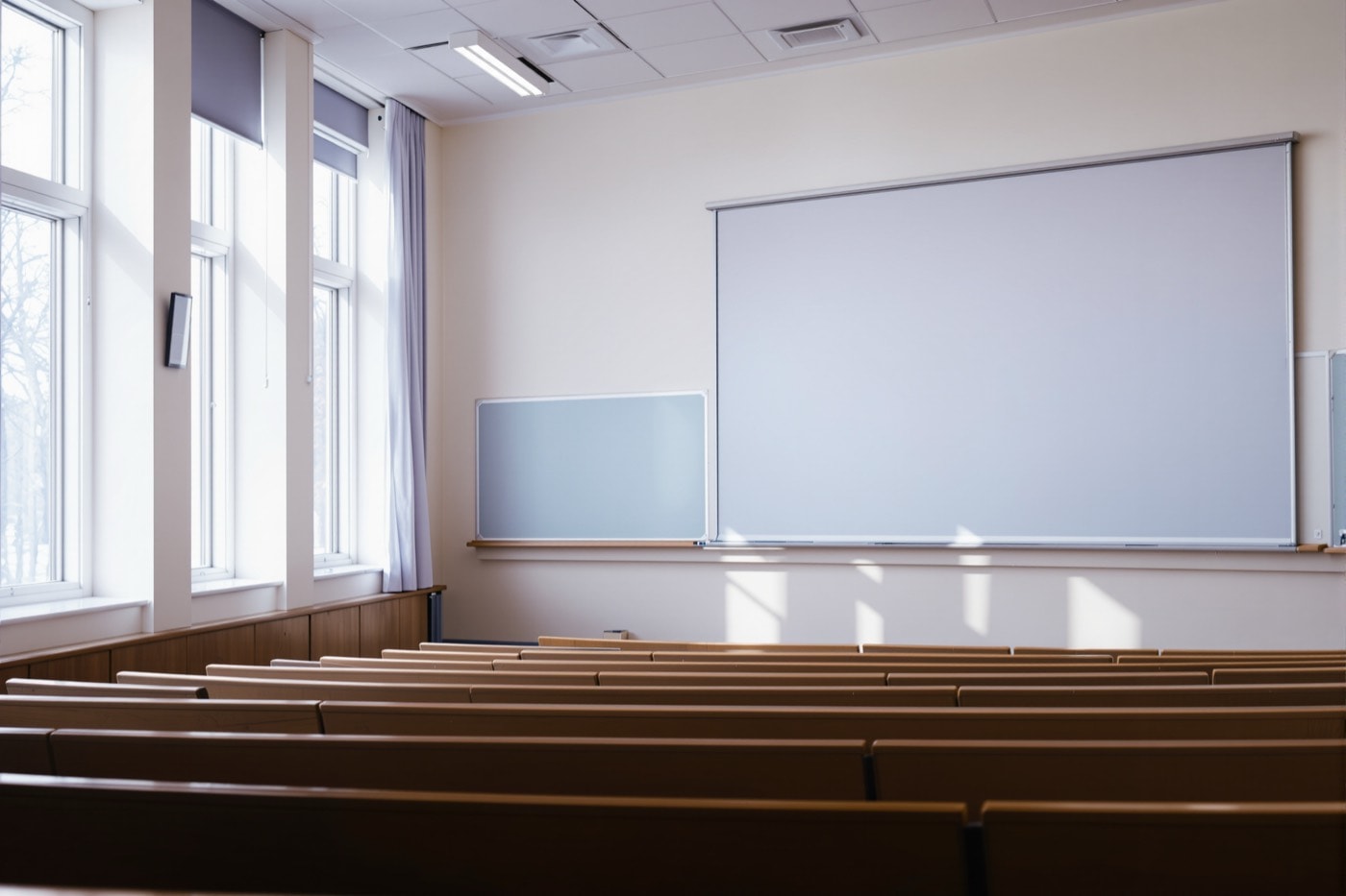 An empty university lecture room with tiered wooden seats and a blank chalkboard in morning light